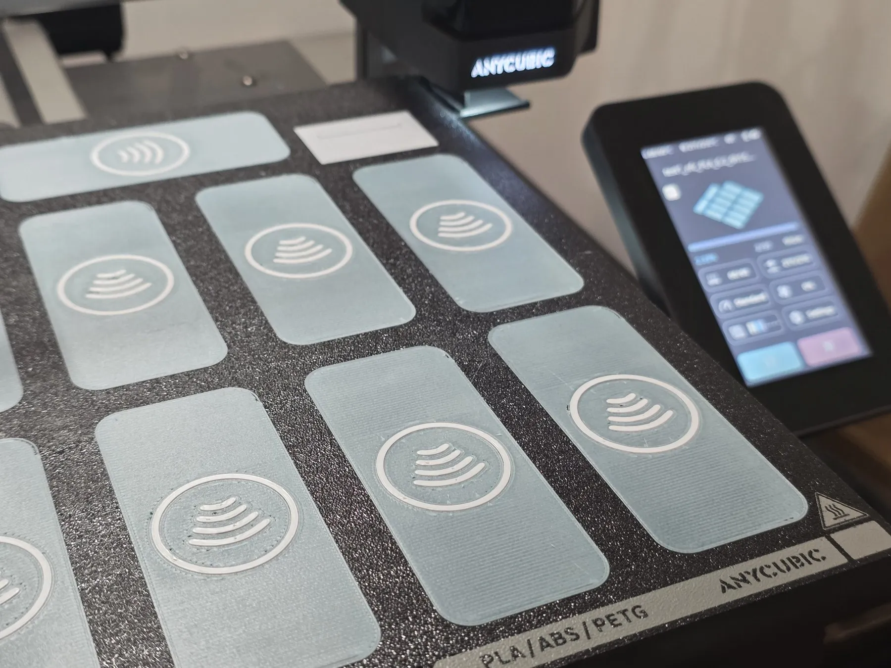 Cama de impresión con seis etiquetas NFC azul claro recién impresas y la pantalla de la impresora encendida